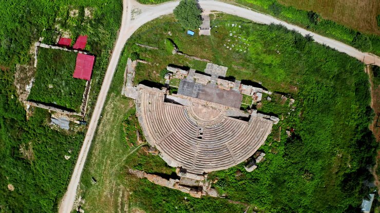 Aerial view of an ancient amphitheater or theater ruins surrounded by green landscape