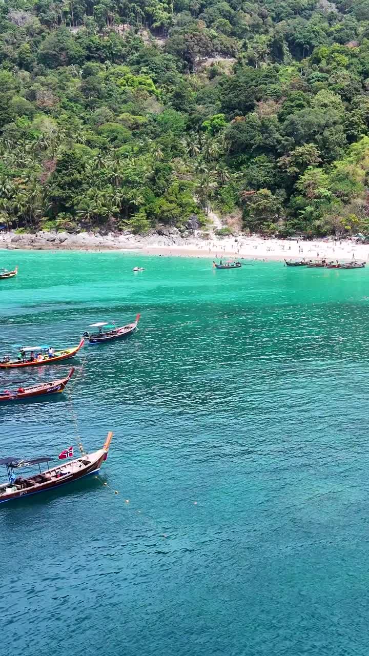 Vista aerea di una vivace spiaggia di Phuket con barche, nuotatori e vegetazione lussureggiante sotto un sole splendente.