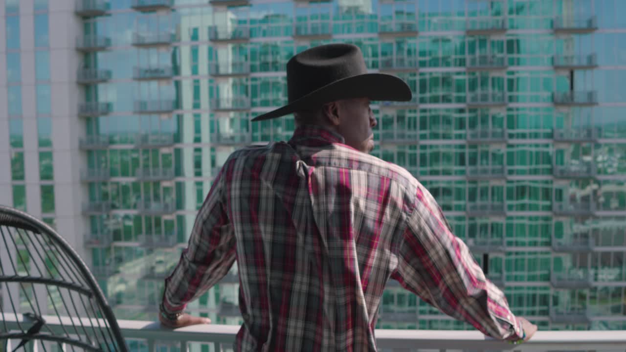 Uomo di colore con cappello da cowboy nero che guarda da un balcone.