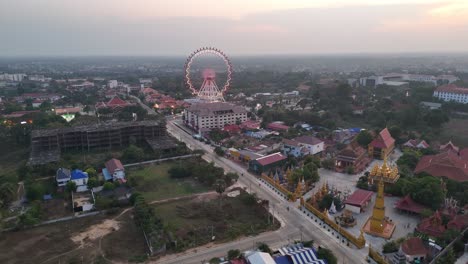 elevated shot of a quiet rural-urban landscape at golden hour. a road extends through scattered homes, trees, and open land, with a distant ferris wheel visible.
