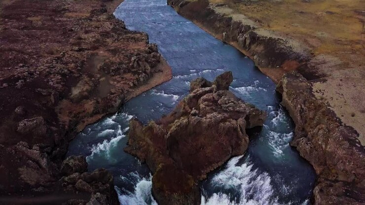 Ripresa aerea con inclinazione verso il basso di un fiume blu che si divide in due cascate gemelle in Islanda.