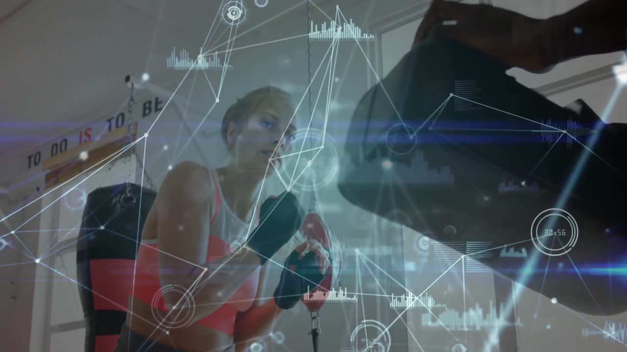 Woman punching heavy bag in gym, displaying digital interface graphics for fitness tech