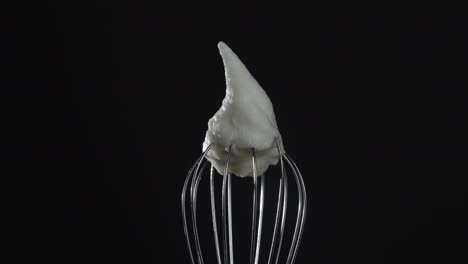 metal whisk with whipped egg whites, isolated on black background