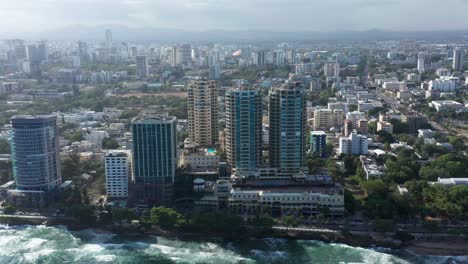 Increible-Vuelo-Esenico-Desde-El-Malecon-De-Santo-Domingo-Donde-Vemos-La-Gran-Ciudad-Y-El-Mar-Caribe,-Muchas-Olas-Y-Clima-Agradable