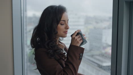 closeup woman drinking coffee looking on city from office window. girl resting.