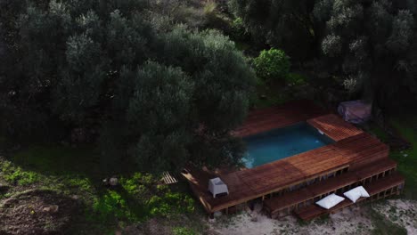 Drone-shot-of-sun-drenched-hilly-landscape-with-swimming-pool-and-trees-and-garden