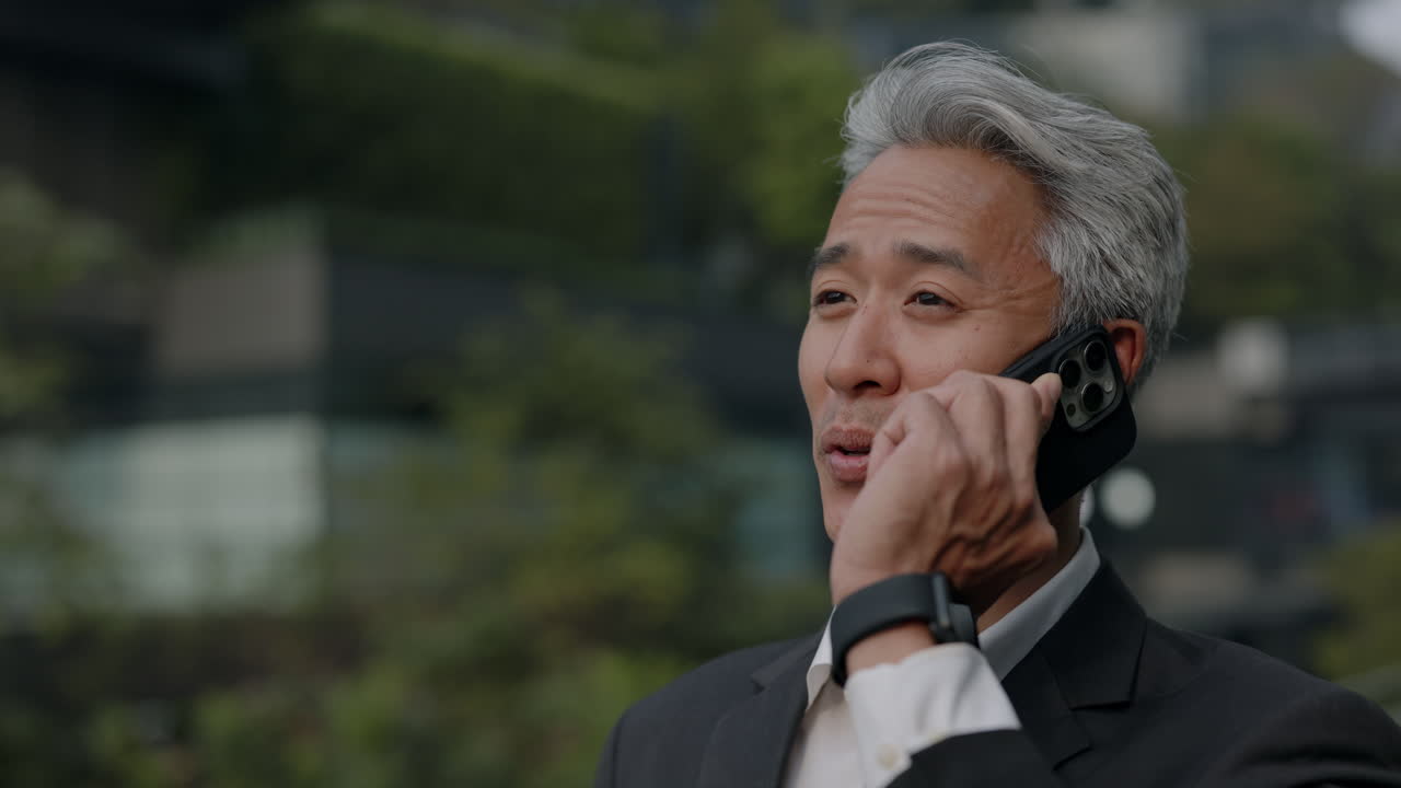 屋外でスマートフォンで話す幸せそうなアジア人ビジネスマン