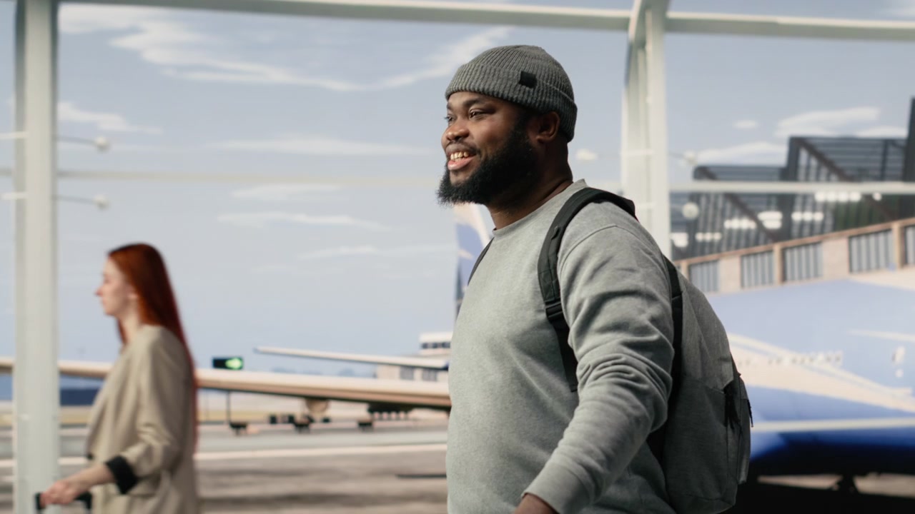 Uomo sorridente che cammina nel terminal dell'aeroporto, con uno zaino e un trolley.