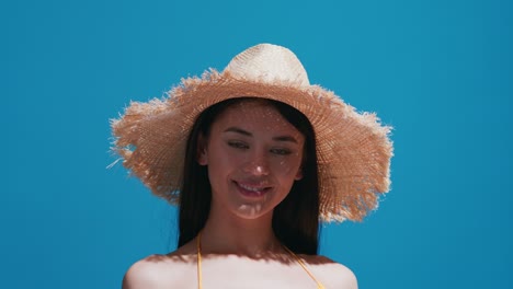 joven con sombrero de paja disfruta del sol contra un fondo azul