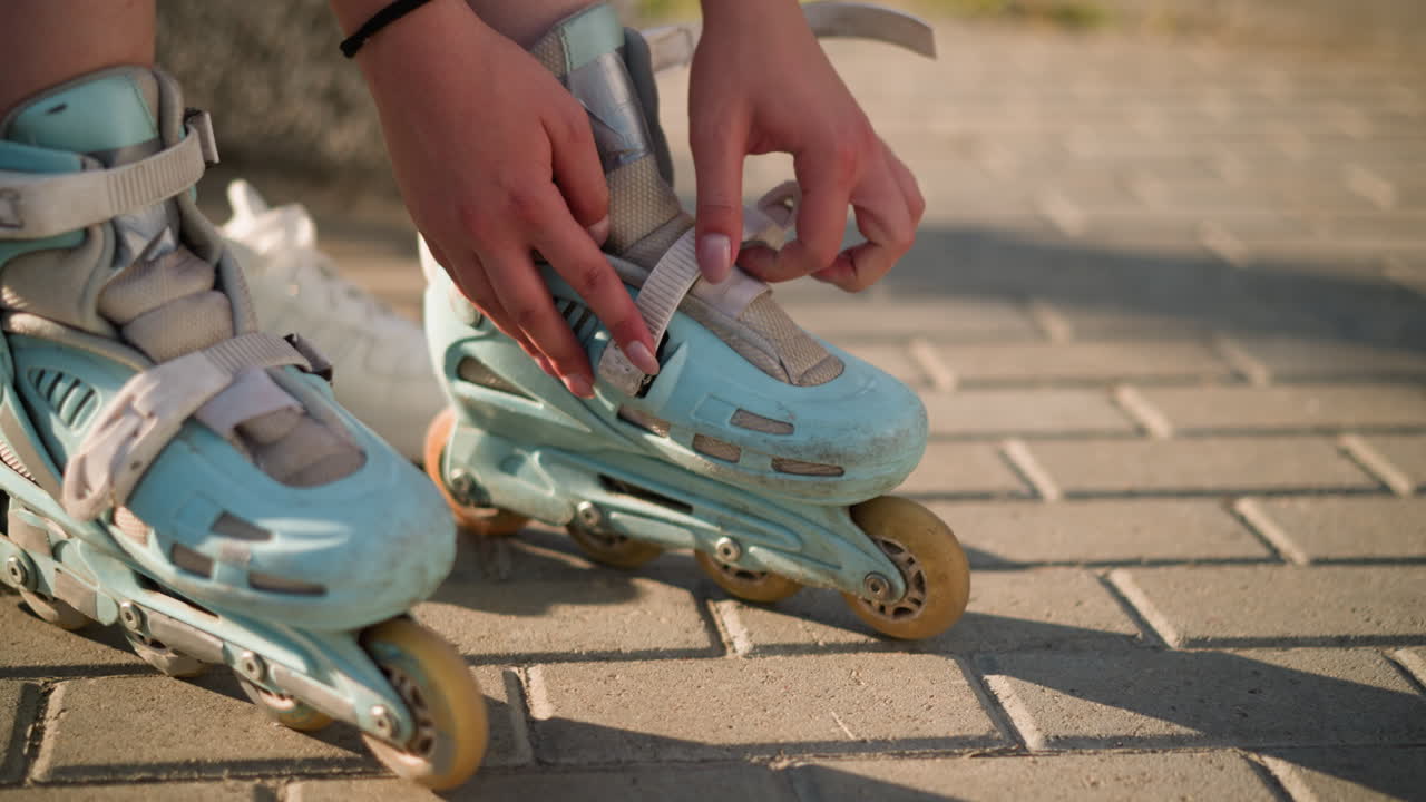 Close-up of individual adjusting strap on left roller skate with careful attention to secure the buckle, capturing detailed hand positioning, white sneakers visible in background