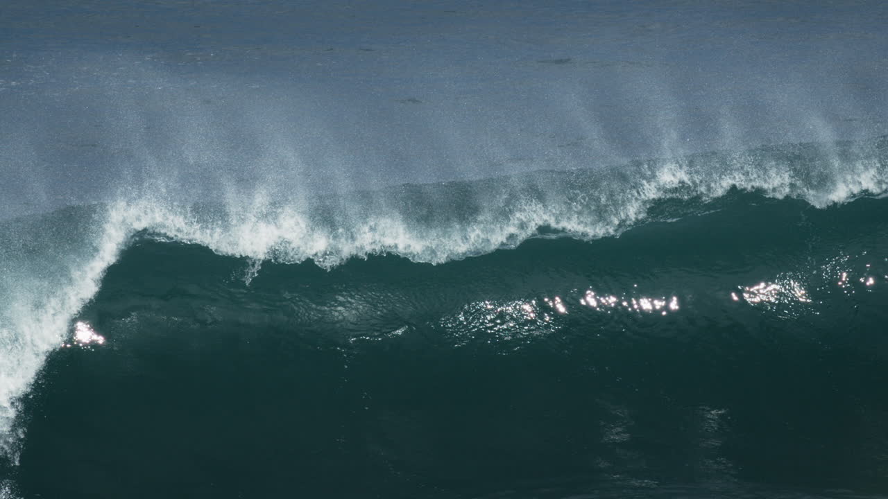 Large turquoise wave rolls with foamy crest under overcast lighting, mist rises off back glistening
