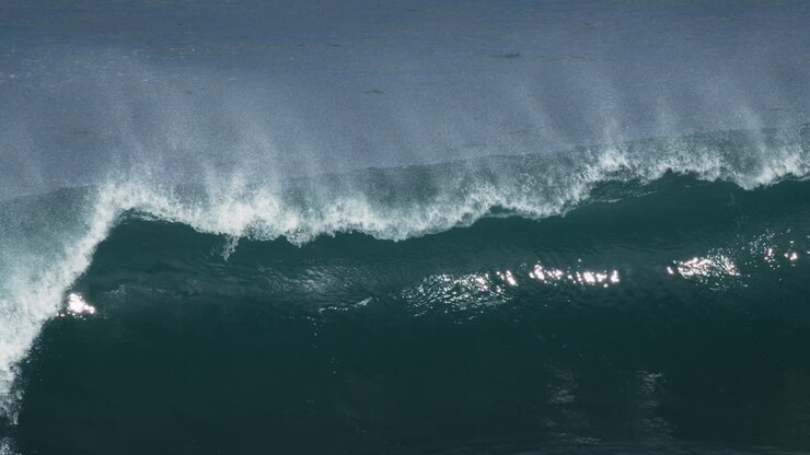 Large turquoise wave rolls with foamy crest under overcast lighting, mist rises off back glistening