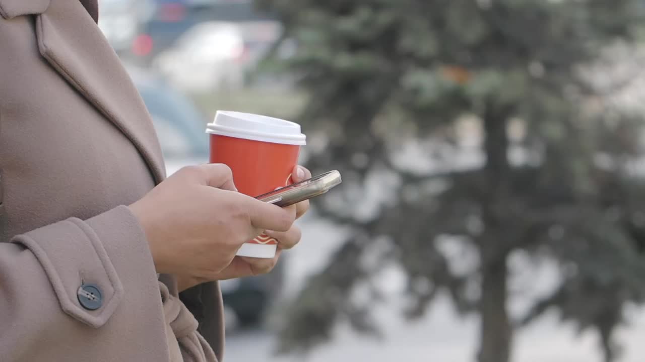 Woman holding coffee cup and smartphone outdoors