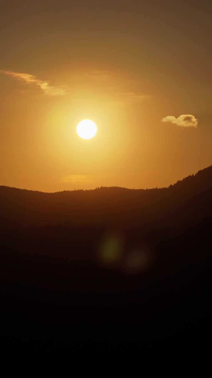 Aerial drone view of the sun setting behind mountain ridges, casting warm golden light across the Carpathians. Vertical