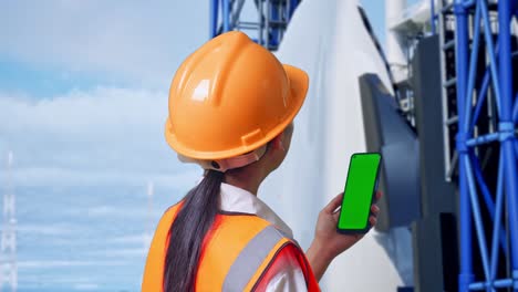 close up back view of asian female engineer with safety helmet working on a green screen smartphone and looking around with space shuttle