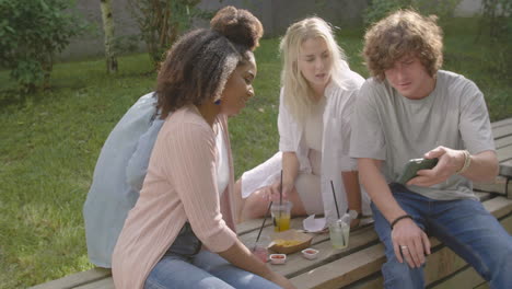 young man showing something interesting on mobile phone to his multiethnic friends in a park 1