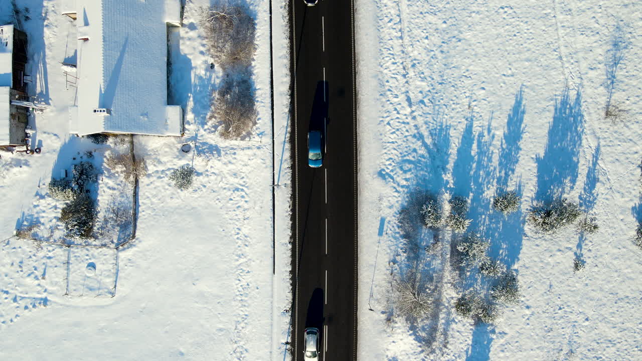 antena de arriba hacia abajo de los coches que circulan por una carretera asfaltada negra rodeada de un paisaje nevado de invierno blanco durante el sol