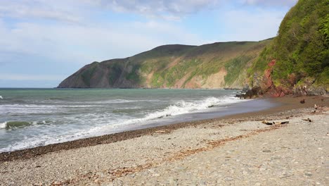 las olas chocan contra las orillas de guijarros de la playa de blacklands en lynmouth mostrando el alcance de la marea con una línea de restos flotantes y desechos en lo alto de la playa