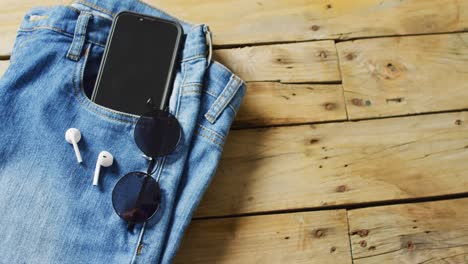 cerrado de vaqueros con teléfono inteligente, auriculares y gafas de sol en fondo de madera con espacio de copia.