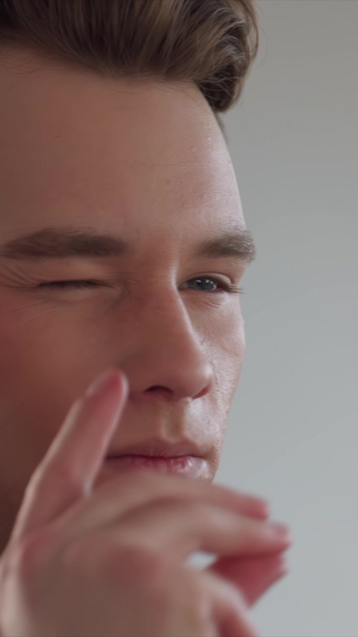 Primo piano di un giovane uomo che si tocca e si sistema ripetutamente i capelli. La sua pelle mostra una leggera acne sul collo con capelli castani acconciati verso l'alto. La scena rimane focalizzata sui movimenti della testa.