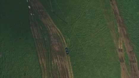 aerial view of a car on a dirt road in a grassy field