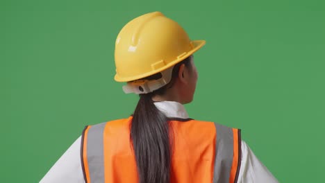 vista de atrás de una ingeniera que usa un casco de seguridad mirando a su alrededor mientras está de pie con los brazos akimbo en el estudio de fondo de la pantalla verde
