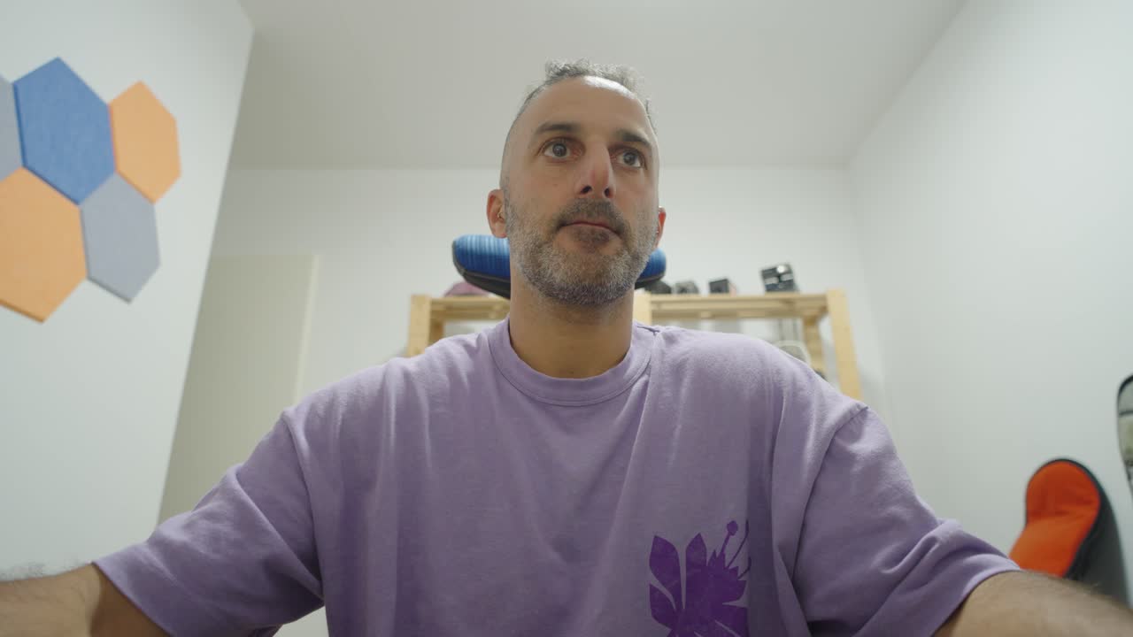 A seated man in a plain room looks up with a serious face, capturing a simple everyday moment of thought and self awareness