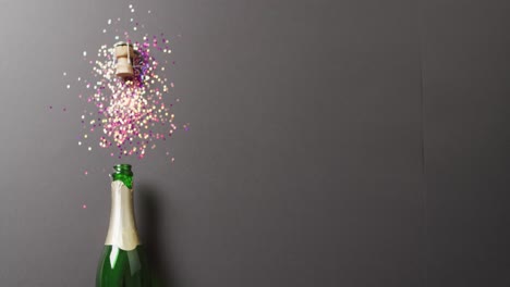 Video-of-vertical-champagne-bottle-and-cork,-with-colourful-glitter-on-black,-with-copy-space