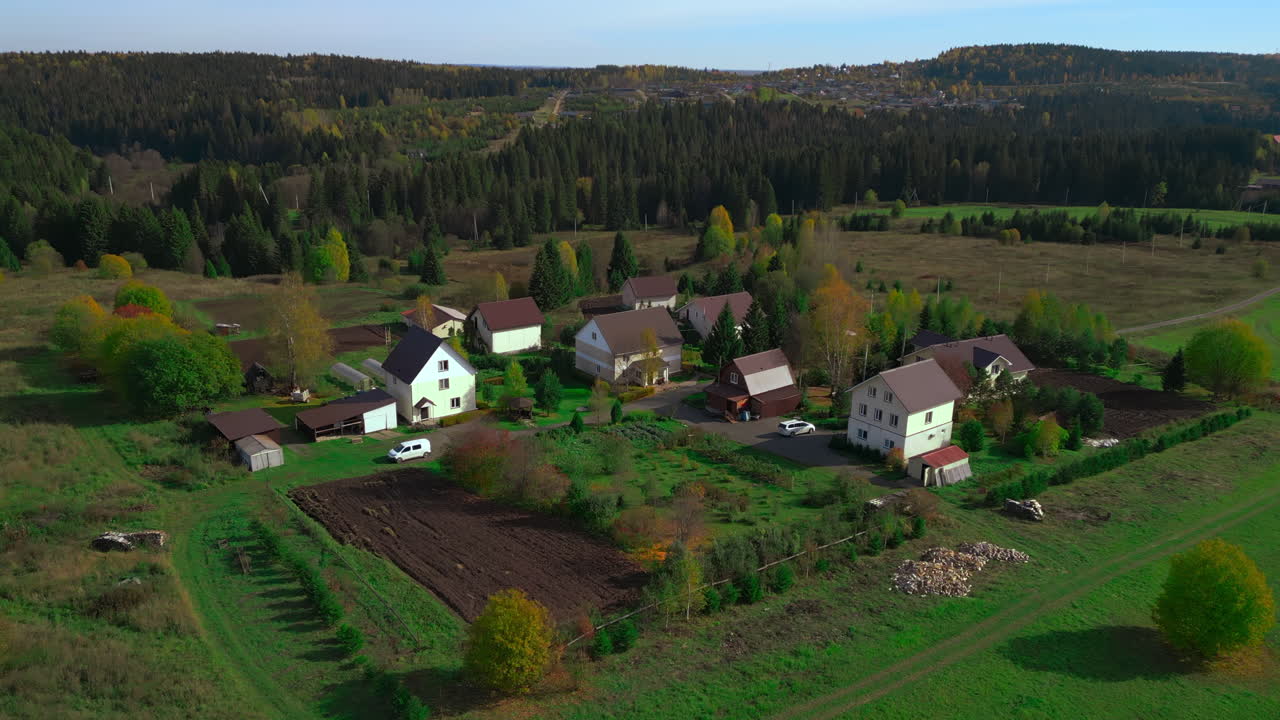 Flyfoto: Høstlandsby med klynger av hus, pløyd mark, spredte hager, hvite hjem og en låve som ligger lunt.