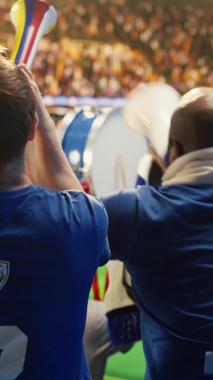 Video verticale: Tifosi di calcio di spalle che sventolano sciarpe e cantano con le vuvuzela.