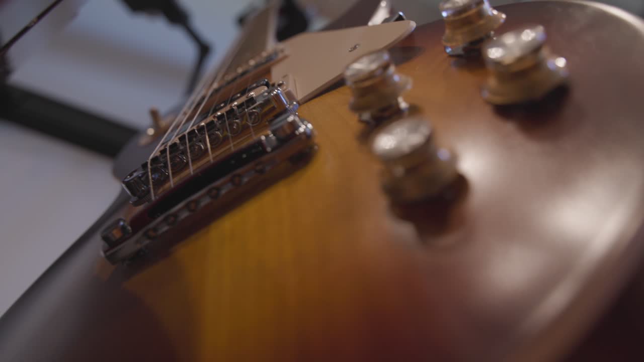Slow motion camera panning across the bottom of electric guitars that are hanging on a wall.