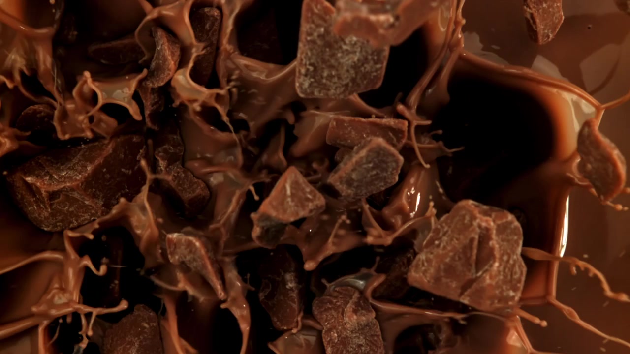 Chokoladestykker, der falder og plasker ned i smeltet flydende chokolade i slow motion