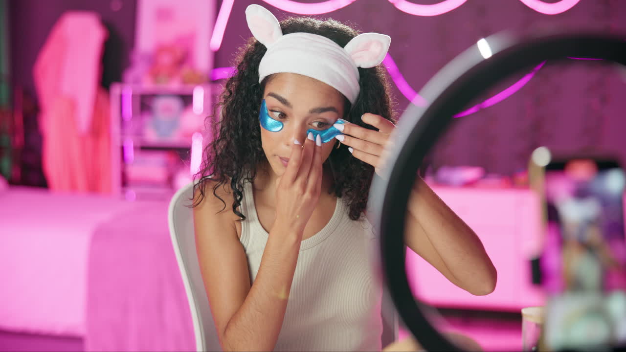 Woman applying eye patches while vlogging in her bedroom