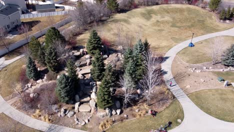 drone shot flying around a children’s rock park and playground in a circle, as kids play together on a sunny spring day after covid-19 lockdown restrictions are lifted