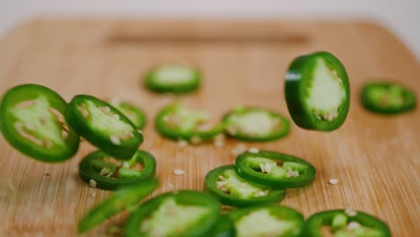 밝은 녹색 jalapeños가 나무 커팅 보드에 떨어지고 더미에 튀고 떨어집니다.