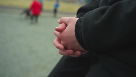 close-up of someone's hands clasped together with a blurred view of children playing in the background