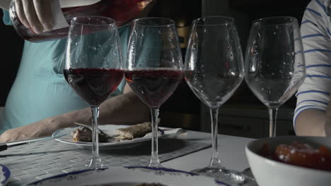 man pouring red wine in four glasses