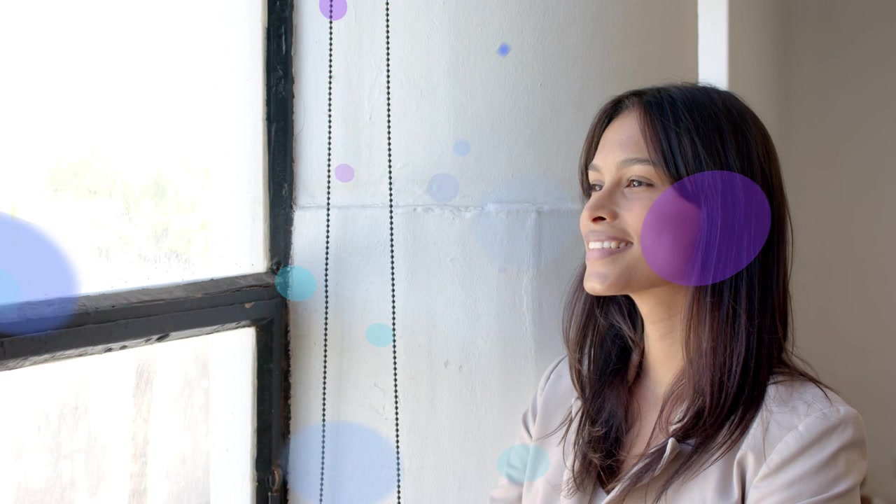 Woman sitting right by window watching circles emerging from left, marketing making her smile