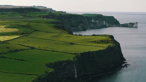 Aerial-Circling-Shot-of-Northern-Ireland-Cliffs,-Ocean,-and-Green-Fields