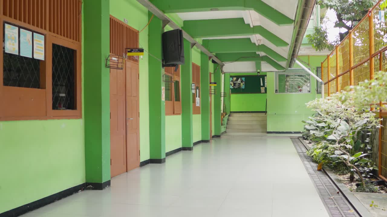 Camera zoom out reveals empty school hallway painted green at SMAN 28 Jakarta, Indonesia, in bright daylight