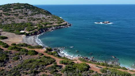 costa de la isla de creta con olas golpeando la playa rodeada de bosques y senderos, cielo azul