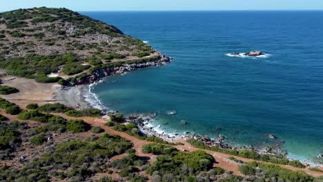 shore of crete island with waves hitting the beach surrounded by forest and trails, blue sky