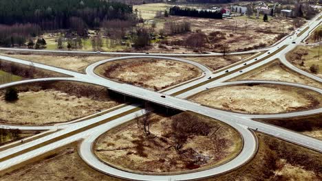 Drone-Aéreo-Vuelo-Lento-Rotonda-Carretera-En-Letonia-Campo-Valmeiras-Tráfico-Panorámico-Paisaje-Amplio,-Campos-Secos,-Fondo-De-La-Ciudad