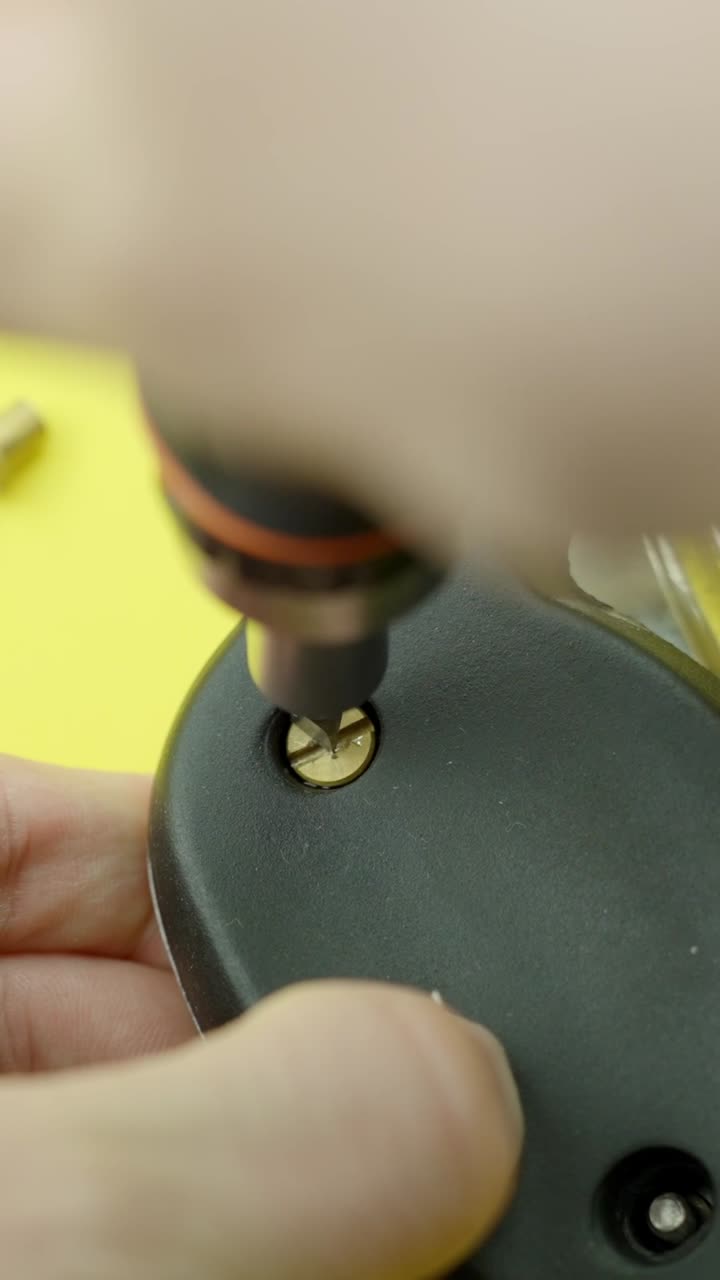 Close-up of screwdriver tightening brass screw into plastic object, vertical