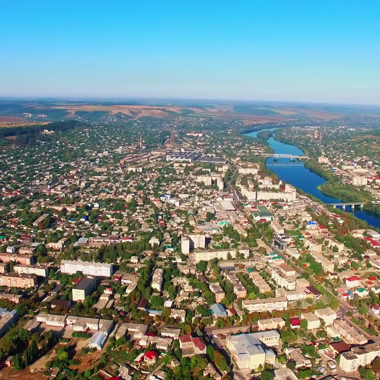 Densely built city landscape with lush greenery. Sunny view of the city on the river banks. Aerial view