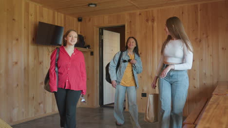 business lady enters cozy wooden resort space smiling and looking around with excitement and curiosity, dressed in white long-sleeve top and jeans, natural light reflecting on wooden table surface