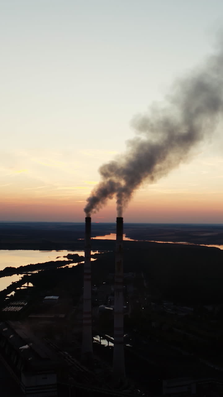 Factory tubes on the sunset background. Smoke from the pipes. Pollution concept. Video from the air. Vertical video