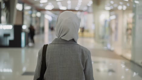 une femme musulmane avec un hijab dans un manteau se promène le long d'un centre commercial