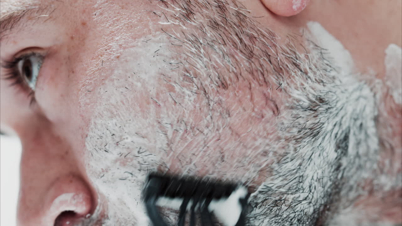 Close up of a man shaving his beard with a razor