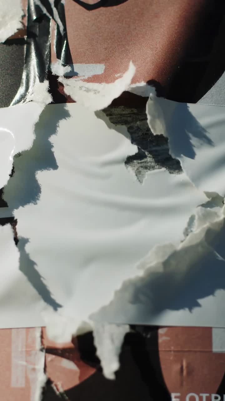 Vertical video: Pulling hand peeling white sheet off wall poster, revealing torso with black strap